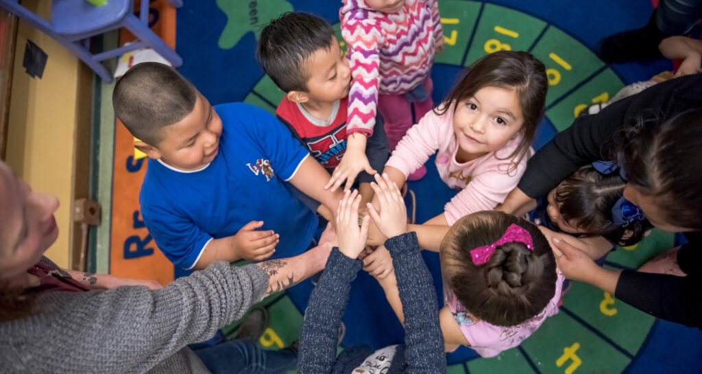 A group of young children standing in a circle with their hands stacked on top of each other in the center.