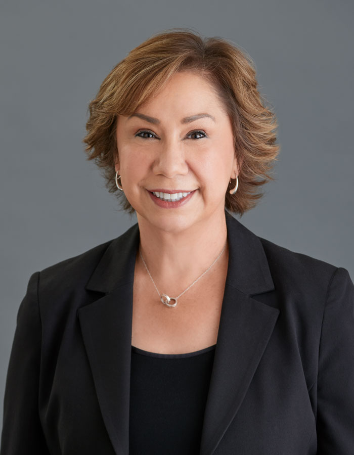 A light skinned middle-aged woman with short brown hair wearing a black blazer, black top, and silver earrings and necklace.