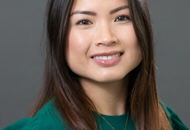 Headshot of Quynh Vu, an Asian woman with long, straight brown hair. She’s smiling at the camera, wearing an emerald green blouse with her favorite necklace.