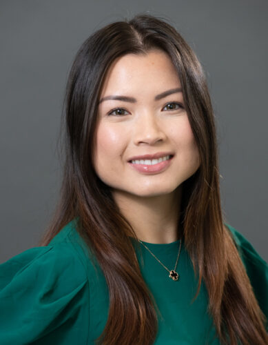 Headshot of Quynh Vu, an Asian woman with long, straight brown hair. She’s smiling at the camera, wearing an emerald green blouse with her favorite necklace.