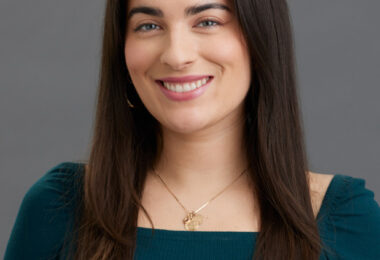Headshot of Serena Solórzano, a white woman with long, straight brown hair and blue eyes. She is wearing an emerald green long-sleeve top and a gold necklace.