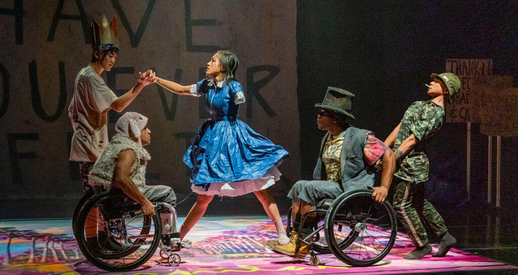 AXIS Dance Company performance of Alice in Californialand. Five dancers are mid-movement on stage, including two using wheelchairs.