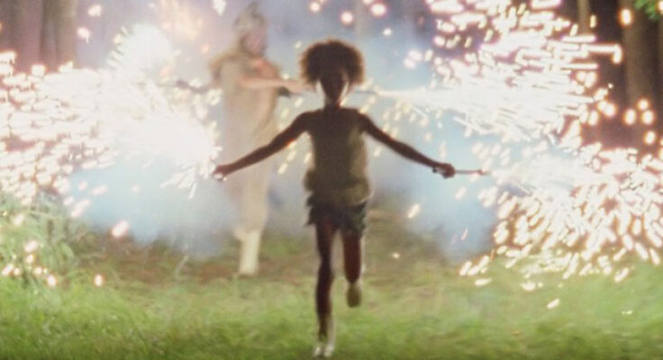 A still image from the "Beasts of the Southern Wild" film where a young Black girl is running towards the camera holding a sparkler in each hand.