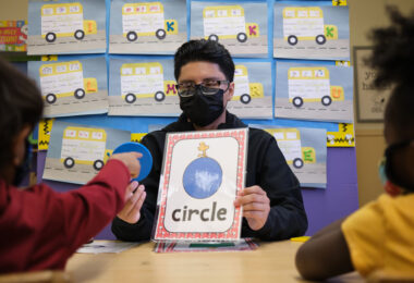 Tutor holding a flash card with a shape and the word circle on it.|Tutor holds a whiteboard with an "R" written on it