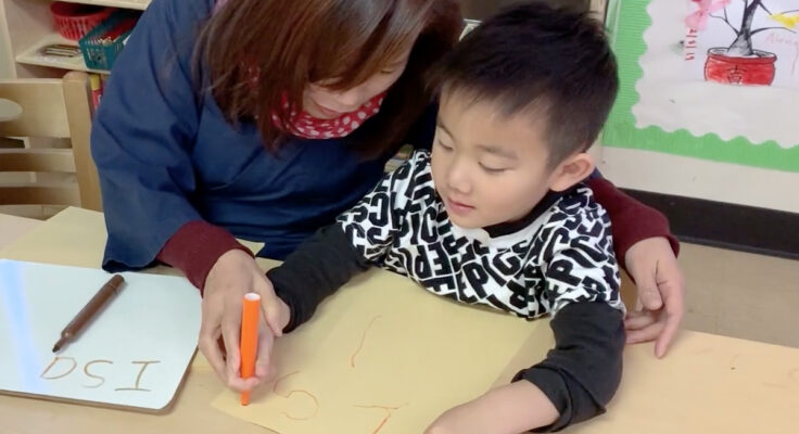 A woman helping a young child with writing.