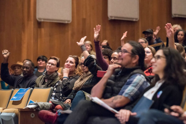 Audience members raising their hands to engage with an artist presentation at the Exploring Public Art Practices Symposium.