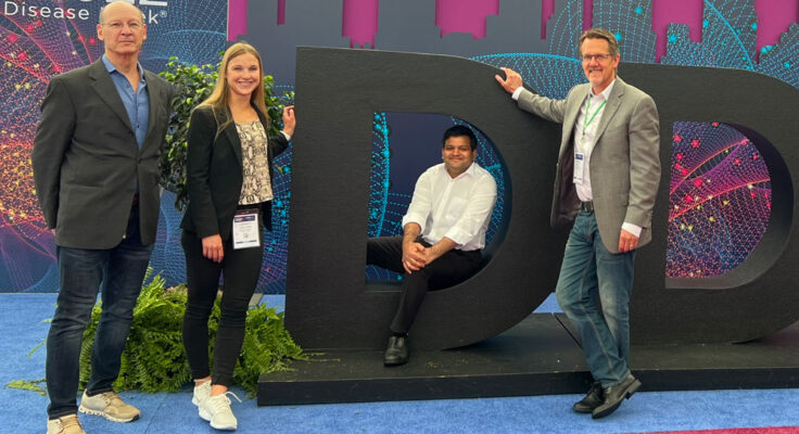 Four people from G-Tech Medical pose in and around a large dimensional letter "D"