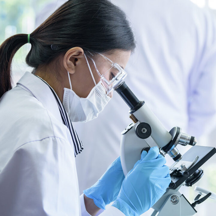 A female scientist in the lab looking into a microscope.
