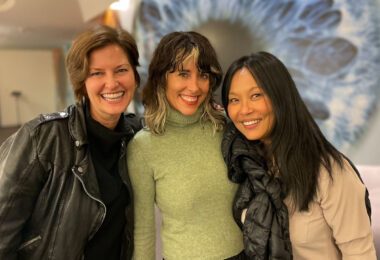 Jen Rainin, Rivkah Beth Medow and Soo-Jeong Kang smiling in front of a blown up image of a blue eye.
