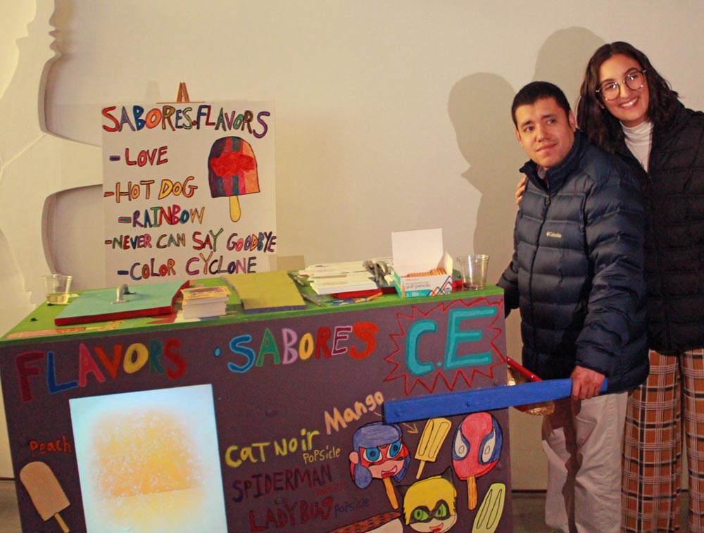 two people smiling next to a Paleta cart painted with colorful letters and illustrations