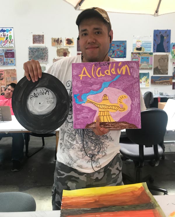 Person holding a vinyl record and sleeve that they have painted and titled "aladdin"