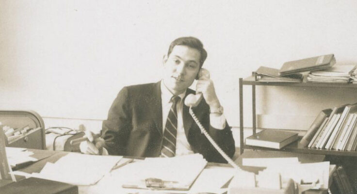Kenneth Rainin pictured at his desk filled with papers as he makes a phone call.