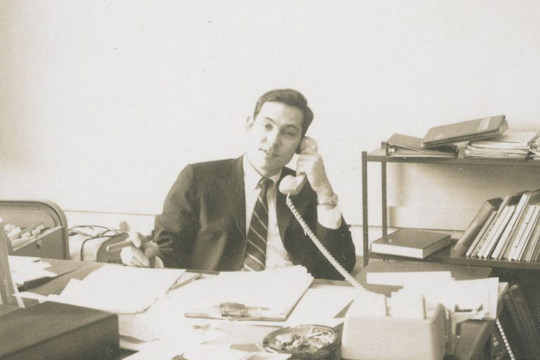 Kenneth Rainin pictured at his desk filled with papers as he makes a phone call.