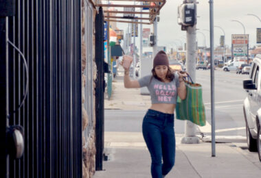 A woman dancing on the sidewalk with a large bag in one hand and an iced coffee in the other.