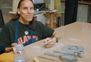 A Creativity Explored artist working with clay and smiling at the camera.