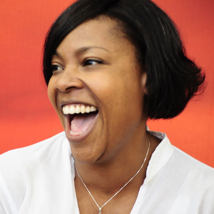 profile of a Black woman with chin length dark hair, smiling joyfully with her mouth open.