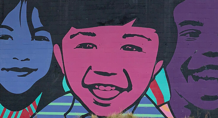 A mural of three children smiling. One if colored blue, another pink and the third purple.
