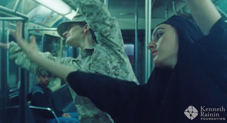 Two people dancing on a train; one wears a military uniform and the other wears a black hijab.