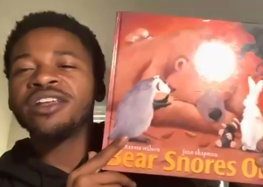 A Men of Color Teaching Fellow holding up a copy of "Bear Snores On" to read aloud to Oakland students.