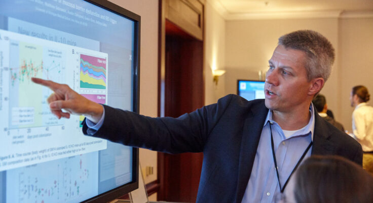 Dr. Eric Martens pointing to his research displayed on a digital poster screen.