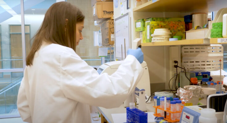 Dr. Jamie Spangler wearing a white lab coat and gloves, working in her lab.