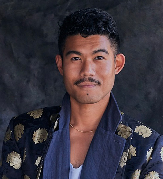 A Filipino man with dark brown hair and a mustache wears a collared, navy blue coat with a gold design.