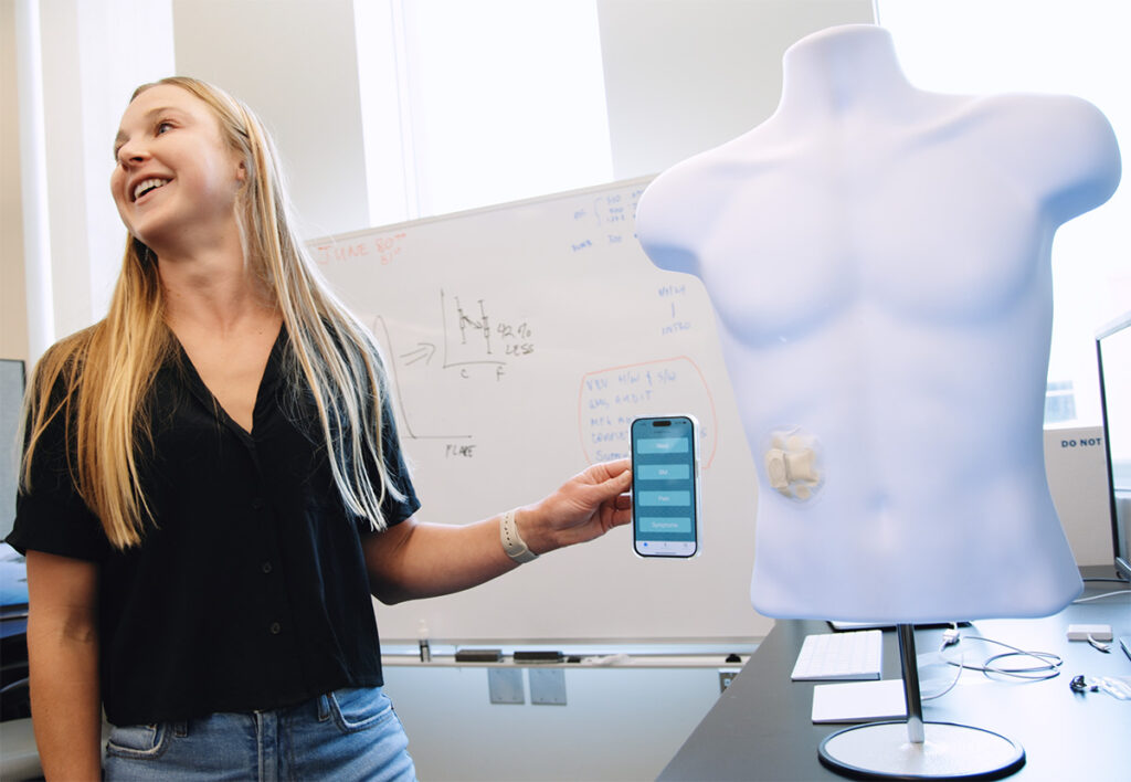 Someone holding up an app on their phone next to a model of a human chest with a patch on the abdomen.