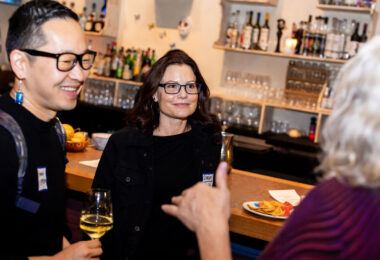 Two people are smiling and facing a person who has their back to the camera