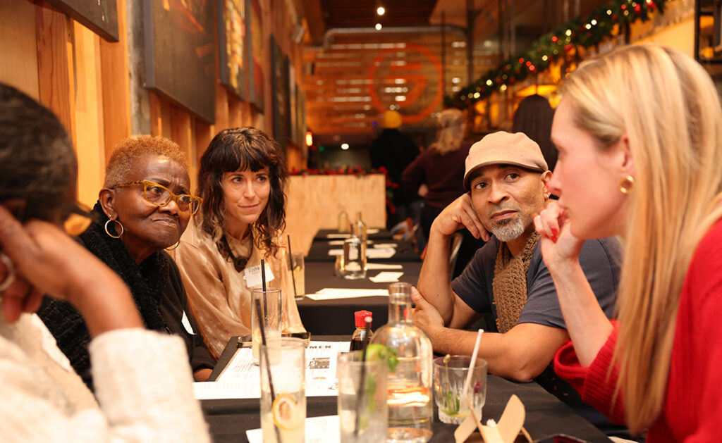 five people seated at a table are talking with each other.