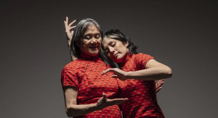 two people, one younger, one older, in matching red short sleeves, stand closely