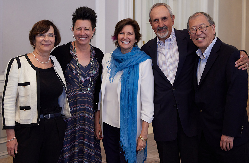 Group of five people stand shoulder to shoulder smiling at the camera.