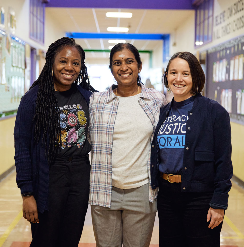 Three adults stand shoulder to shoulder smiling in an elementary school hallway.