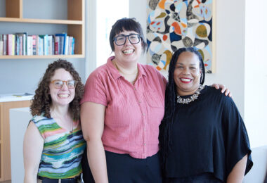 Three people standing closely posing and smiling for the camera.