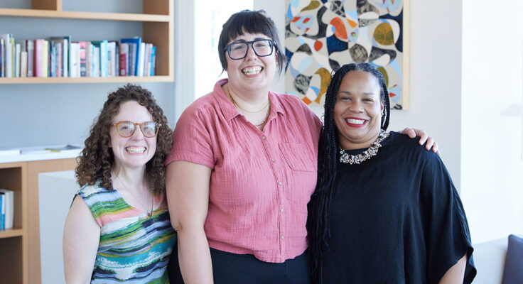 Three people standing closely posing and smiling for the camera.