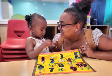 An adult and young child huddle closely, while the child works on a number game.