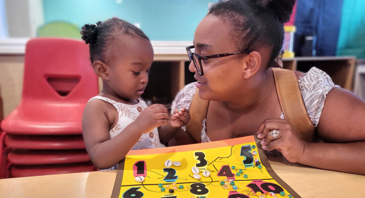 An adult and young child huddle closely, while the child works on a number game.