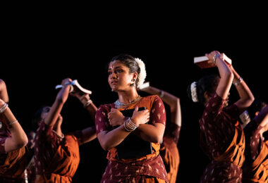 In the foreground, a hopeful dancer gazes outward, clutching a book close to her body. In the background, five other dancers are captured in motion, symbolizing struggle and labor.