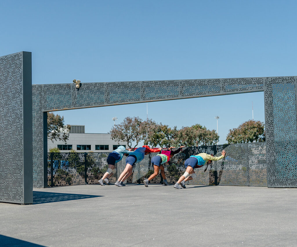 Four people shown pushing against a metal structure.