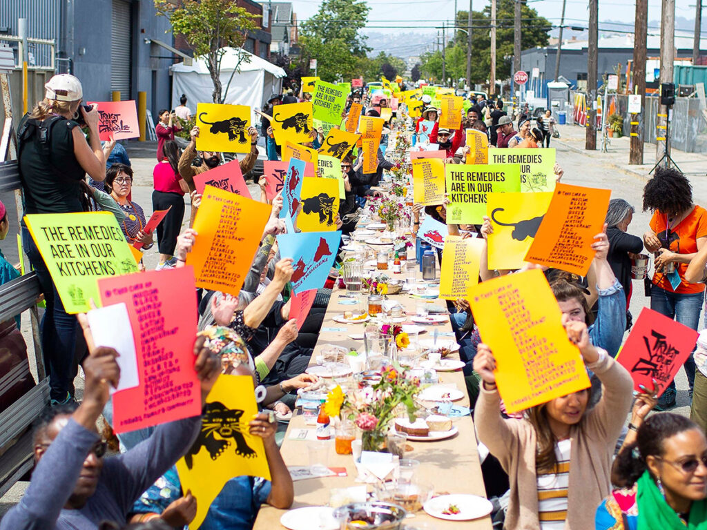 A large group of people seated on two sides of a long table, holding up colorful signs.