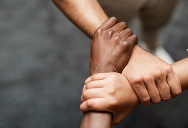 Three arms interlocked to form a triangle, demonstrating uniting in strength and solidarity.