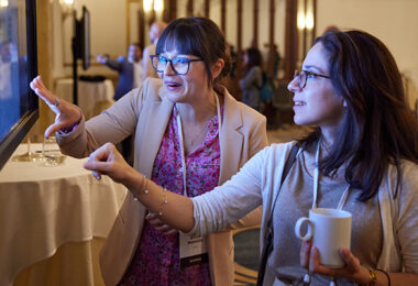 Two people excitedly pointing at a large screen displaying a digital research poster.