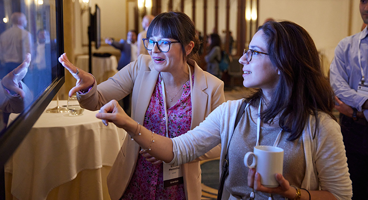 Two people excitedly pointing at a large screen displaying a digital research poster.