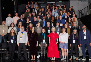 A group of about 60 people standing in tiered rows stand smiling at the camera.