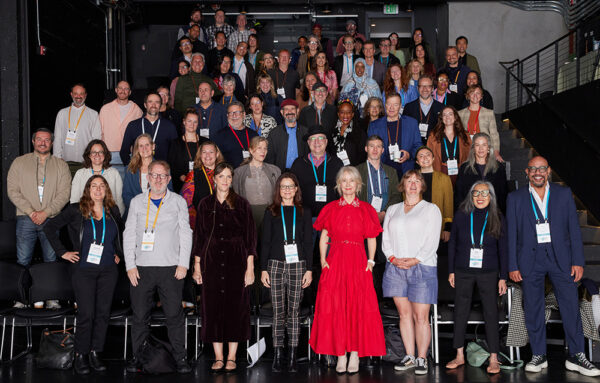A group of about 60 people standing in tiered rows stand smiling at the camera.