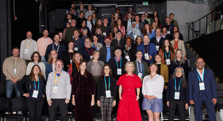 A group of about 60 people standing in tiered rows stand smiling at the camera.