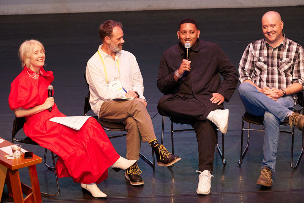 Four people are seated on a stage looking happily at the audience, which is out of frame.