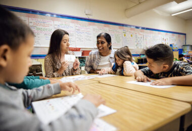 Four students look at an adult who is holding a flash card with a lowercase 'd' on it.
