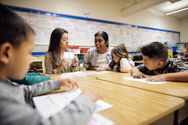 Four students look at an adult who is holding a flash card with a lowercase 'd' on it.