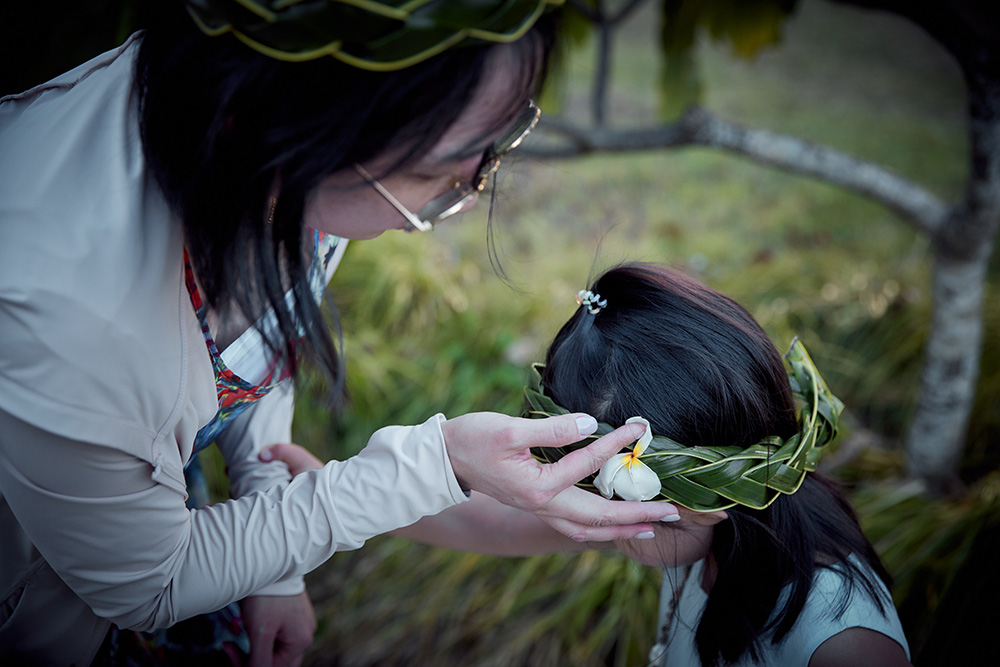 An adult adjusts the braided palm leaf crown on a young child.