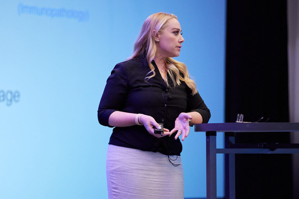Dr. Janelle Ayres speaking in front of a projector screen.